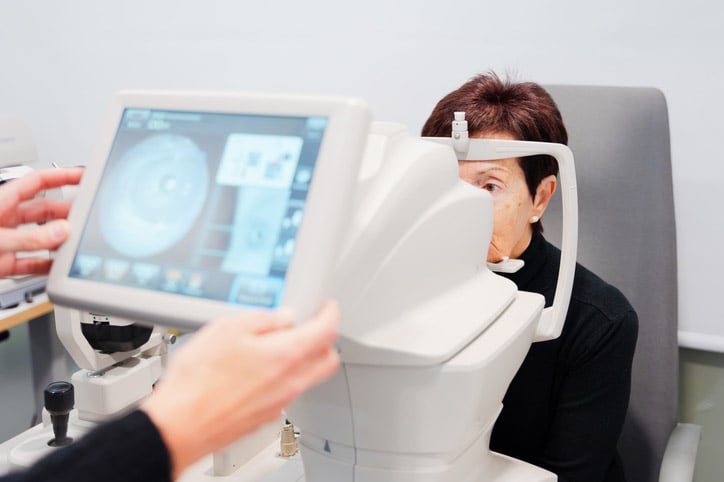 A patient sits for an eye exam using an ophthalmic imaging device.