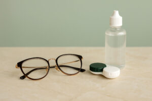 glasses vs. contacts, which is better, modern eyeglasses beside a contact lens case and solution on an upscale tabletop, soft green background, horizontal 4:6