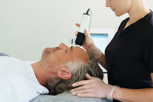 A surgeon performs CO₂ laser resurfacing on an adult man lying comfortably in a treatment chair, using a handheld laser device to rejuvenate facial skin.