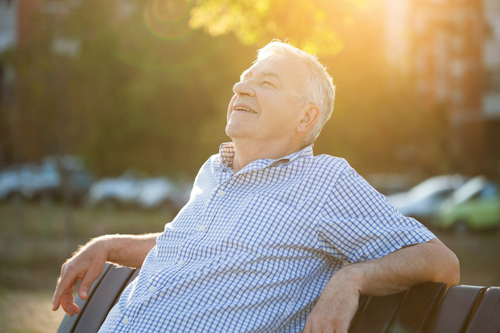 Older man sitting on a park bench in bright sunlight, illustrating long-term sun exposure and cataract risk.