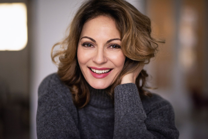 Smiling middle-aged woman with smooth skin and natural facial volume, representing results often achieved with Botox and dermal fillers.