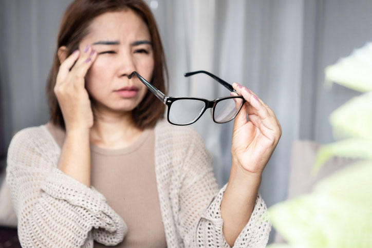 Farsightedness example showing blurred close-up vision as a woman struggles to focus on glasses held nearby.