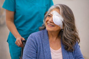 Older woman in wheelchair wearing a taped plastic eye shield and smiling back at her nurse after retinal detachment treatments at Vantage Eye Center