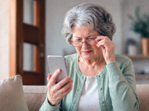 Senior woman with cataracts wonders how cataracts affect your vision; squinting at her phone, from Vantage Eye Center.