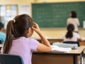 Young girl squinting at the classroom chalkboard because of blurry distance vision, illustrating nearsightedness treatment options at Vantage Eye Center.
